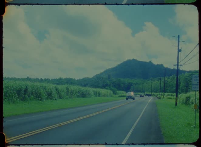 Cars drive along a country road with mountains in the background