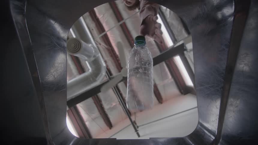 A persons hand drops a bottle into a hole on the top of a metal recycling bin