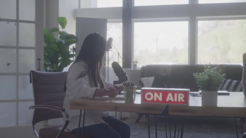 Two people talk in front of a microphone with an on air sign lit