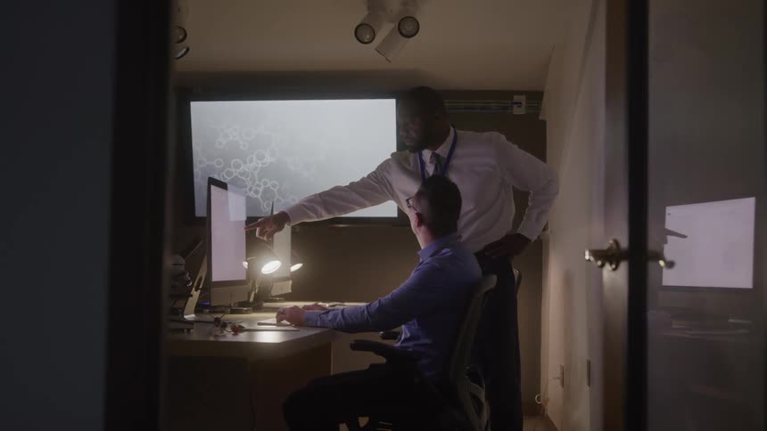Two professionals analyze data on a computer inside a dark room