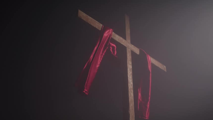 A wooden cross indoors partially covered by a waving red cloth surrounded by smoke