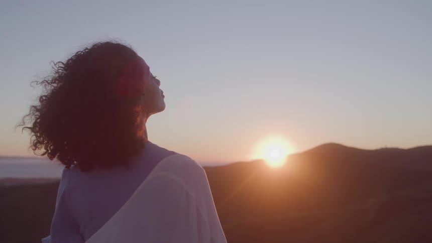 The wind blows the womans hair as the sun rises