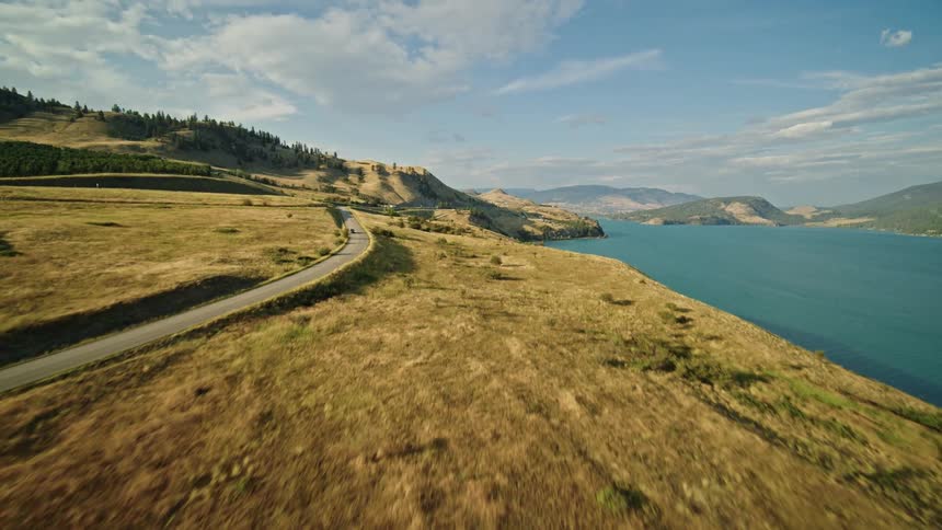 A winding road cuts through grasslands with a lake and mountains behind