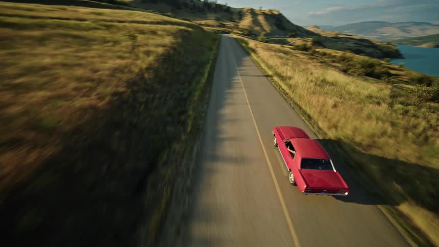 Person drives a vehicle on a highway roughly paralleling a lake bordering the mountains