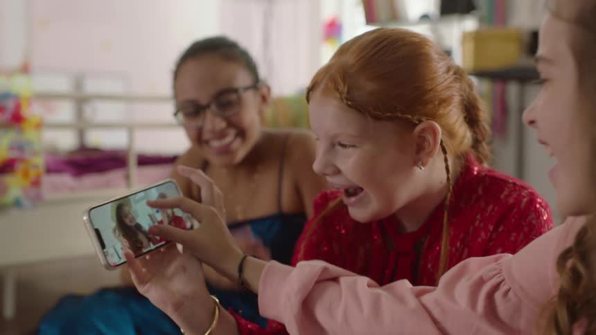 Three girls looking at a phone screen and laughing in a room setting