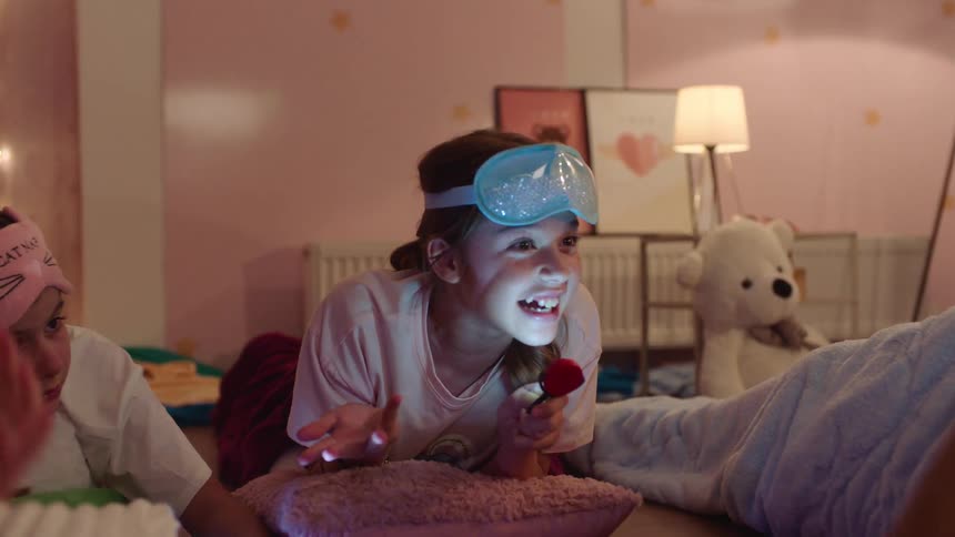 Kids at a sleepover tell spooky stories in a bedroom using a flashlight