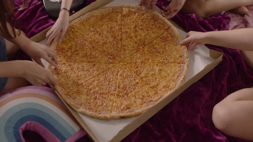 Four girls grabbing one slice of pizza each the pizza is on top of a blanket
