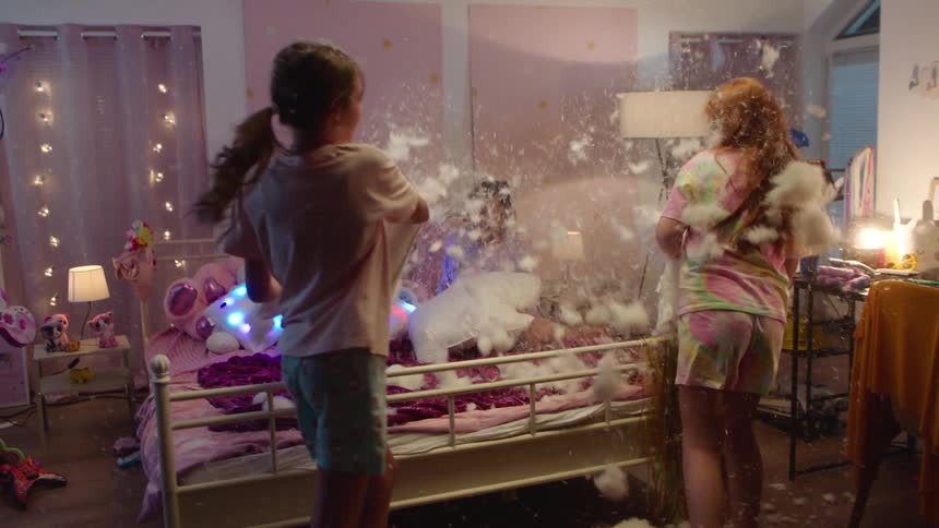 Four girls have a fun pillow fight together in a bedroom