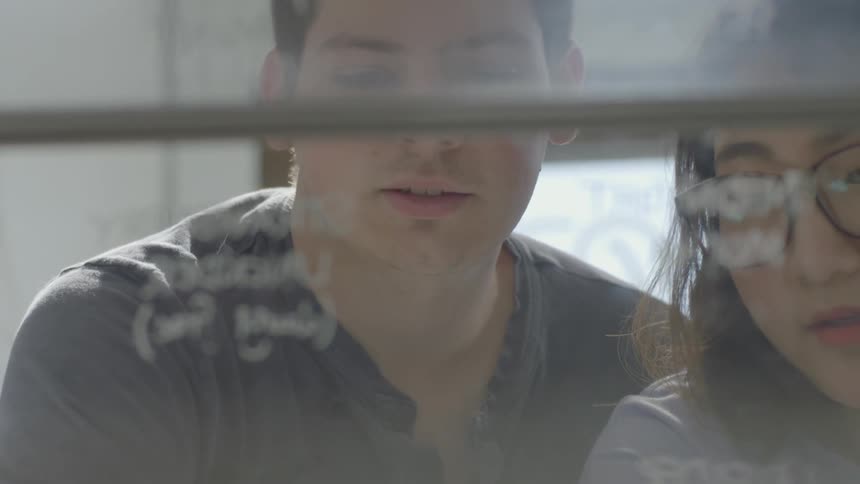 Man and woman point to words written on glass
