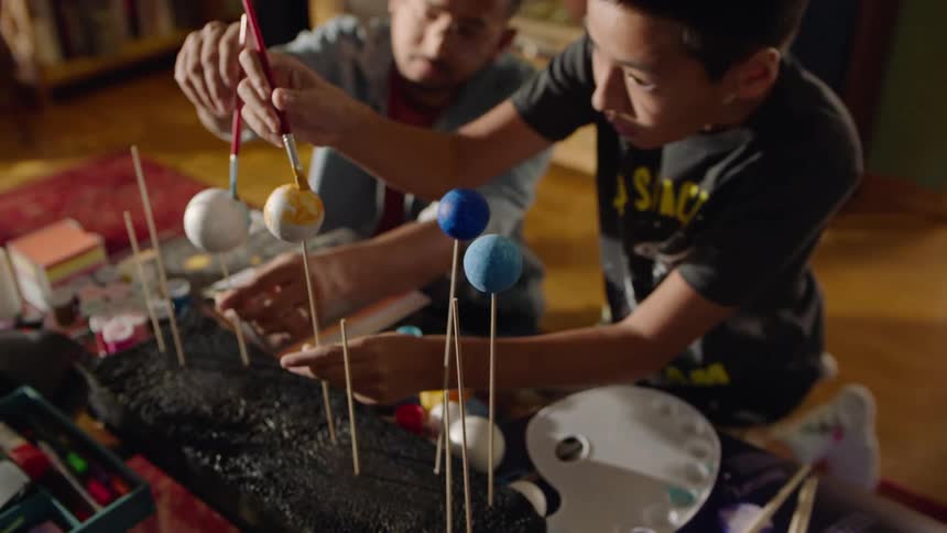 A father and son work together on a solar system model at home