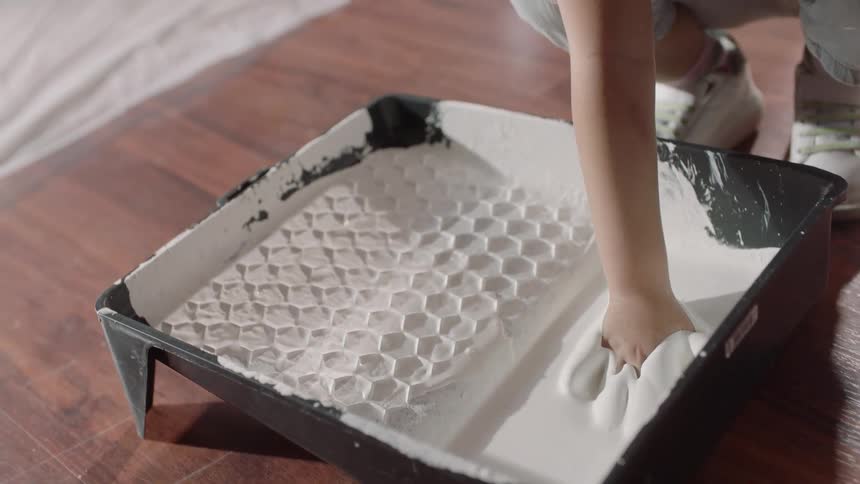 A person kneels next to a paint tray and submerges the hand into white paint