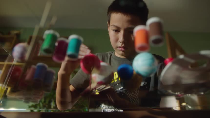 A shot focuses on a young boy painting on a pane of glass with bottles of paint visible through the glass the camera is positioned from a low angle as the boy concentrates on his work