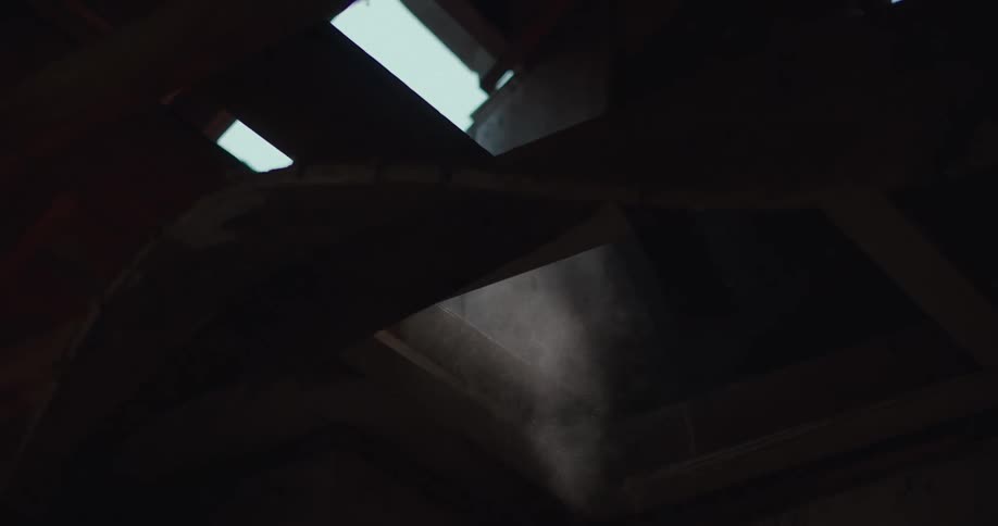 A view from a low angle shows dust floating through a shaft of light that shines through a dark wooden attic space
