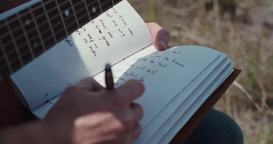 A persons hands write in a notebook with a guitar fretboard visible
