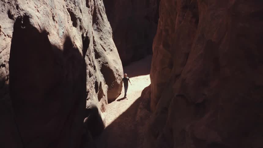 A solitary figure walks through a sunlit slot canyon surrounded by towering rock formations