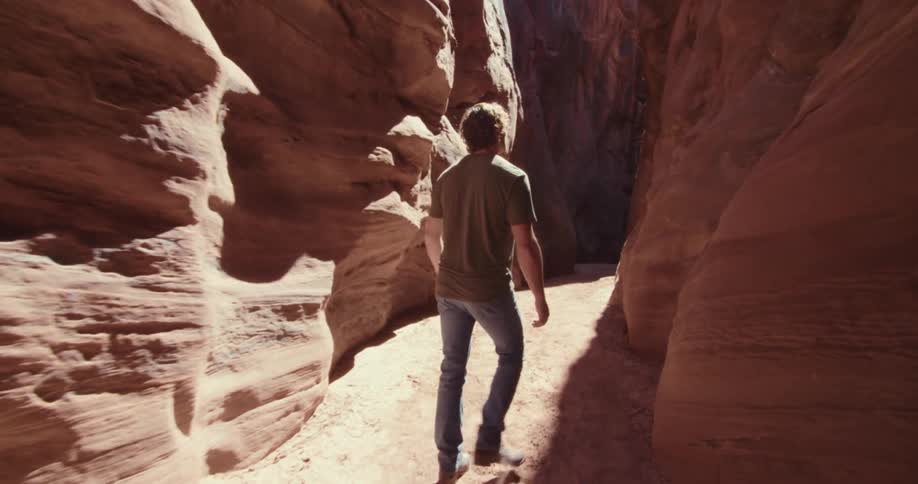 A young person walking through an open cave in a canyon on a sunny day