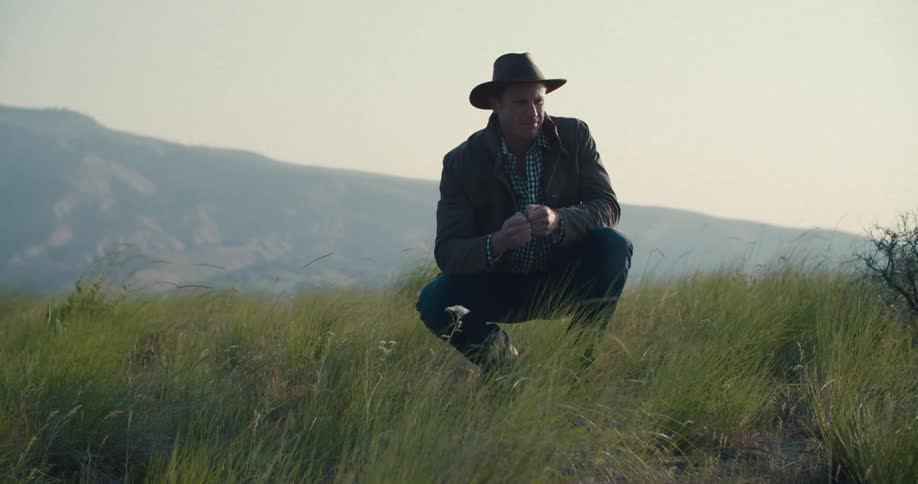 Man in hat crouching on a mountain
