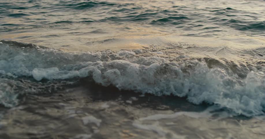 Calm ocean waves lap against the shore at sunset as the suns warm light glimmers on the waters surface the waves crash gently creating small bursts of white foam
