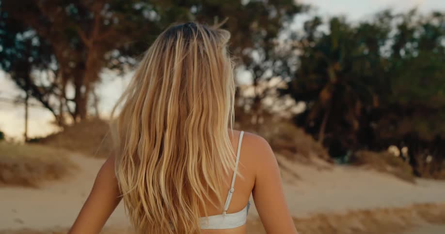 A woman walks on a beach and turns her head to look and smile at the camera