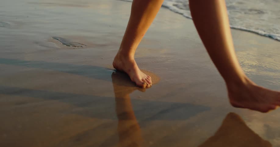 Bare feet of a woman walking on the wet sand of the beach