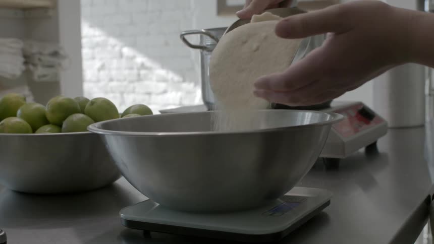 A person pours a scoop of sugar into a silver bowl