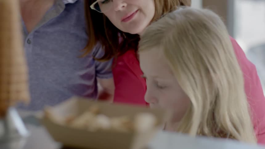 A young girl with her family is trying a flavor of ice-cream in a shop