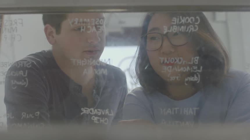 Man and woman talking in front of a glass pane with writing on it