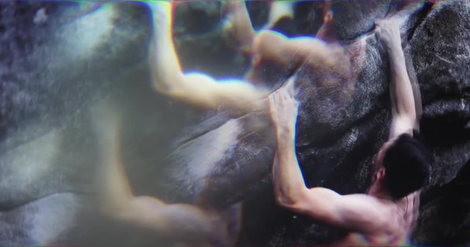 A distorted video shows a closeup of a shirtless man rock climbing the camera focuses on his hands and feet as he grips the dark rock with a refracted lens effect creating a kaleidoscopelike view of the scene
