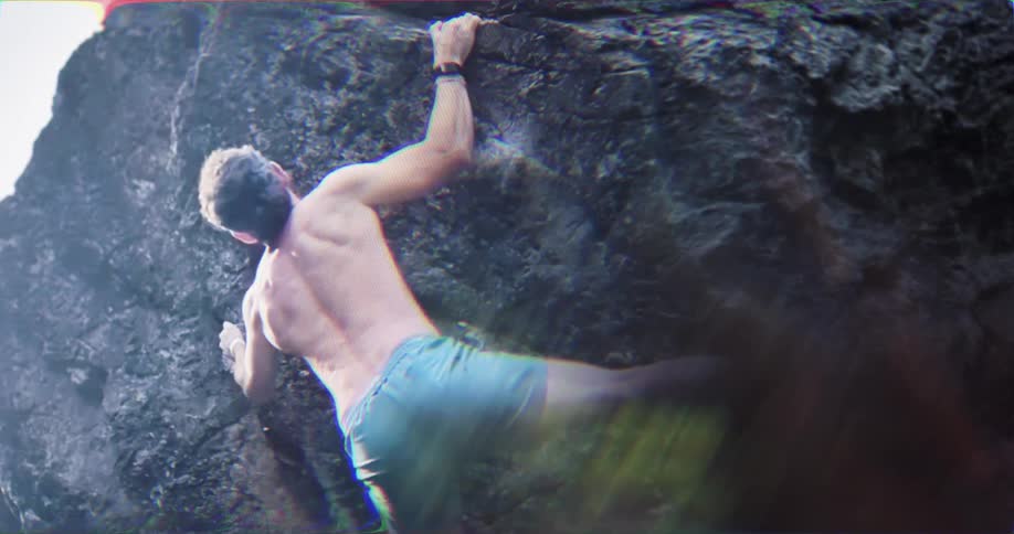Bearded man struggling to climb on rocks with another man behind him offering help outdoors during day time