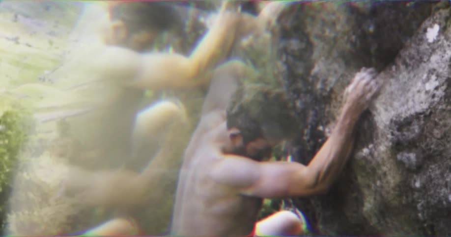 Shirtless man climbing the rock face of a mountain
