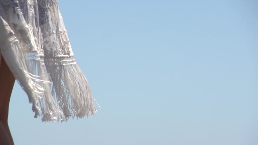 A white dress blows in the wind as a woman stands