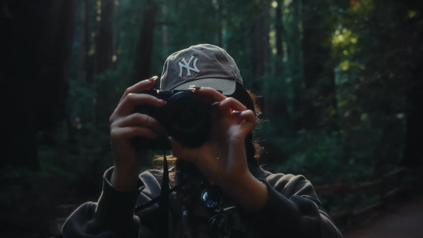 Person wearing a cap holds a camera in the forest