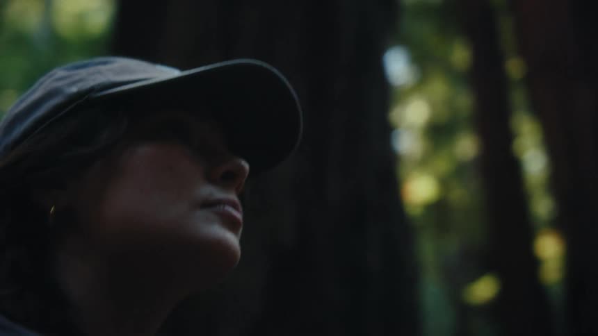 Woman wearing a cap uses a camera in the middle of the forest