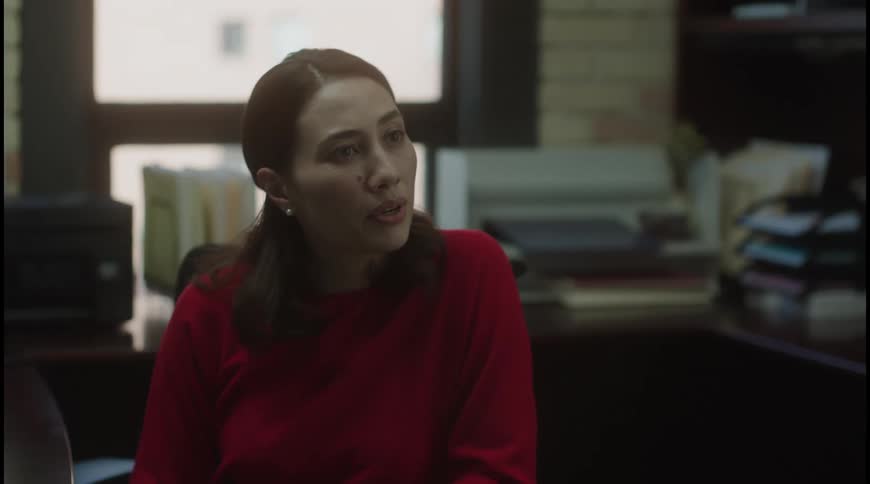 Young woman indoors wearing a red blouse sitting on a chair at an office talking