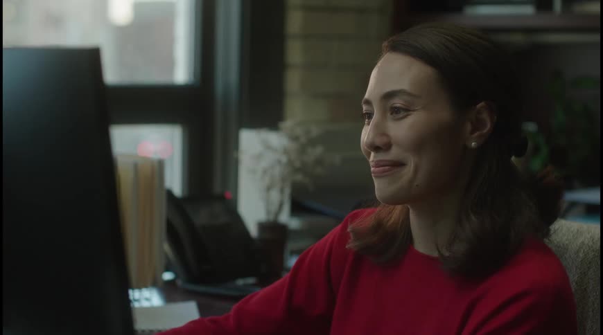 Woman in red smiles while working at her office desk