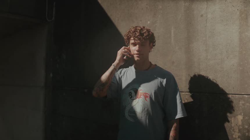 Man in a grey t-shirt with tattoos walks while talking on the phone