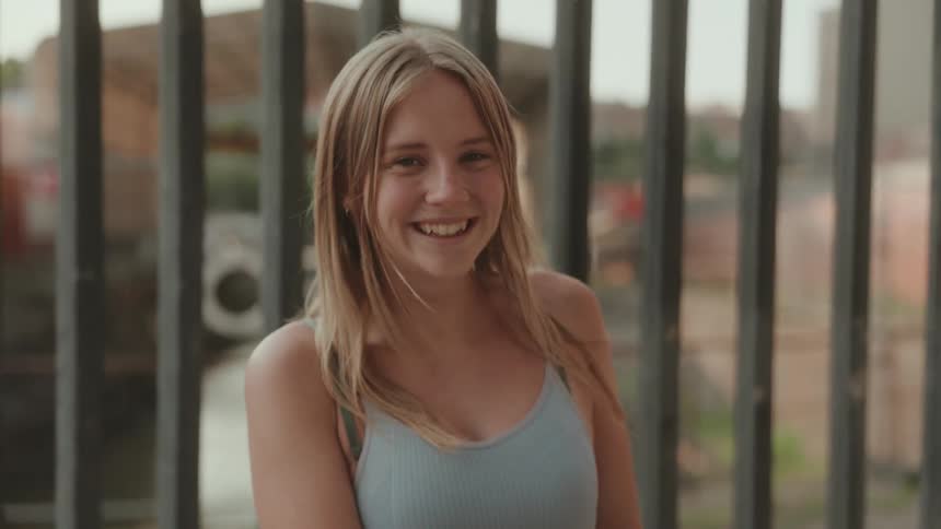 A young woman is leaning against a fence smiling laughing and clapping