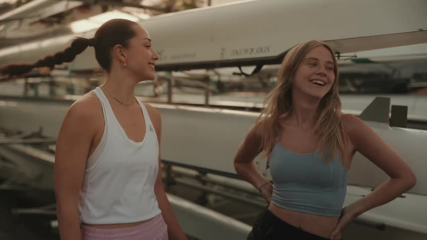 Two young athletes celebrate smiling with a high five near rowing boats