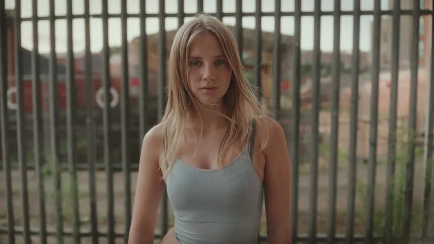Portrait of young woman standing in front of a metal fence looking at the camera