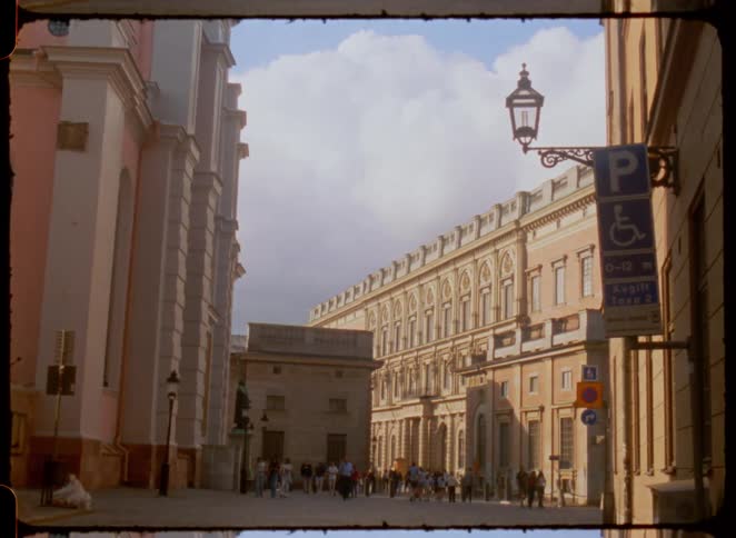 People walk on a street between two buildings in a city