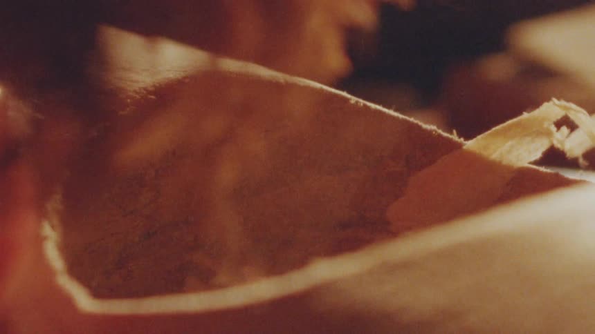 Woodworker blowing wood shavings out of a carved hole in a piece of wood indoors