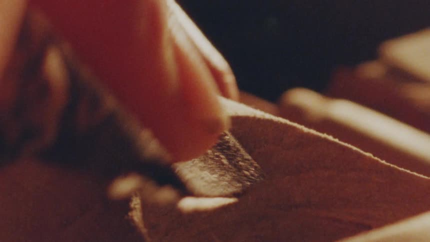 Finger holds sandpaper rubbing the wooden surface