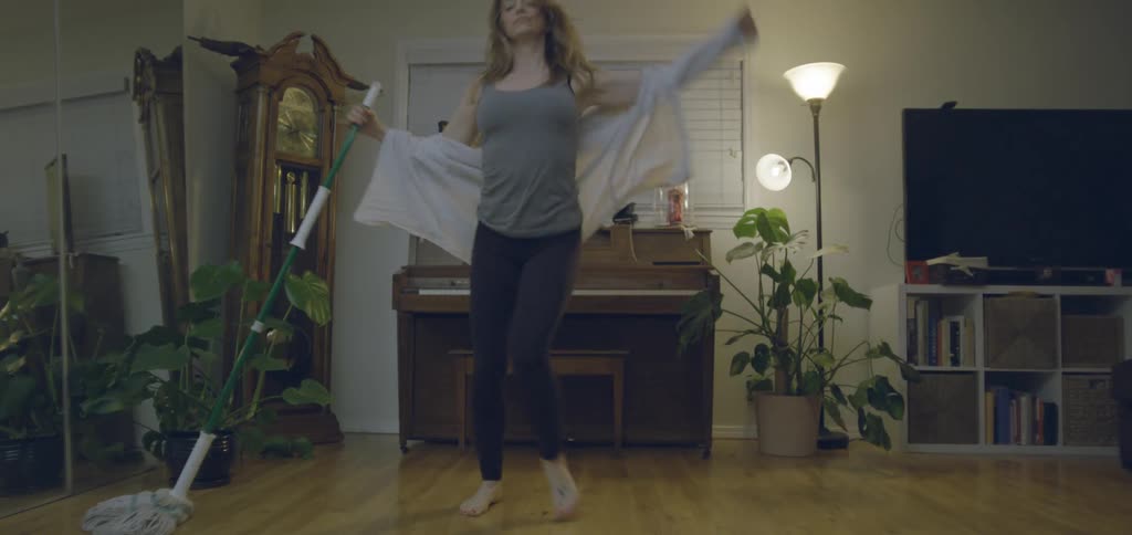 Young woman dancing and laughing while mopping the floor in a living room indoors