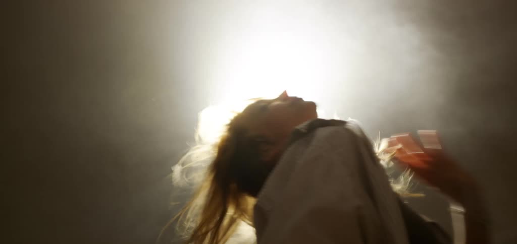 Blonde woman wearing a shirt dancing and holding a stick in her hand indoors