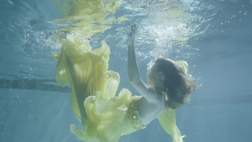 A woman in a yellow dress falls underwater