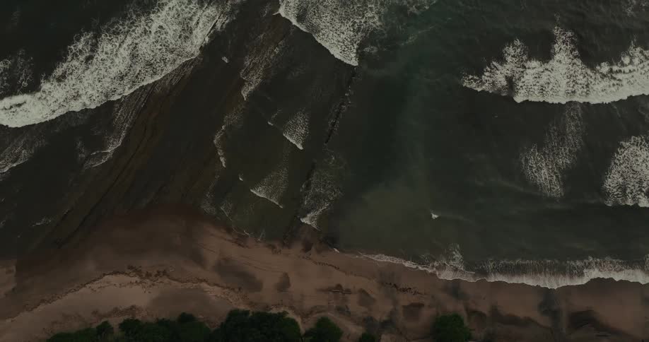 Birds eye view waves rolling in ocean towards sandy shoreline