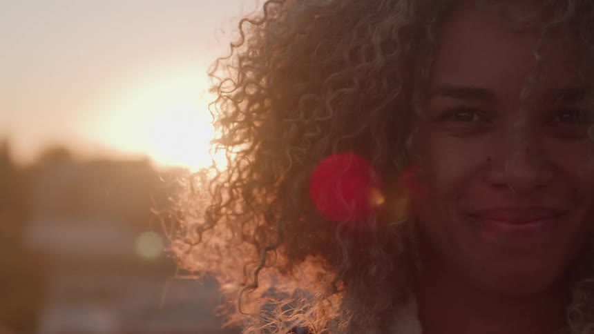Woman with curly hair lit by the sunset light smiles