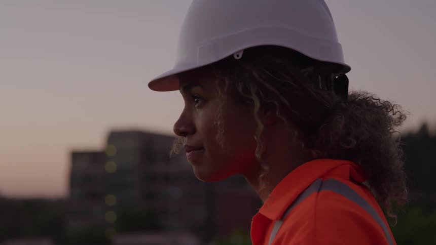 Female construction worker standing on top of a building on an urban area outdoors during dusk or dawn