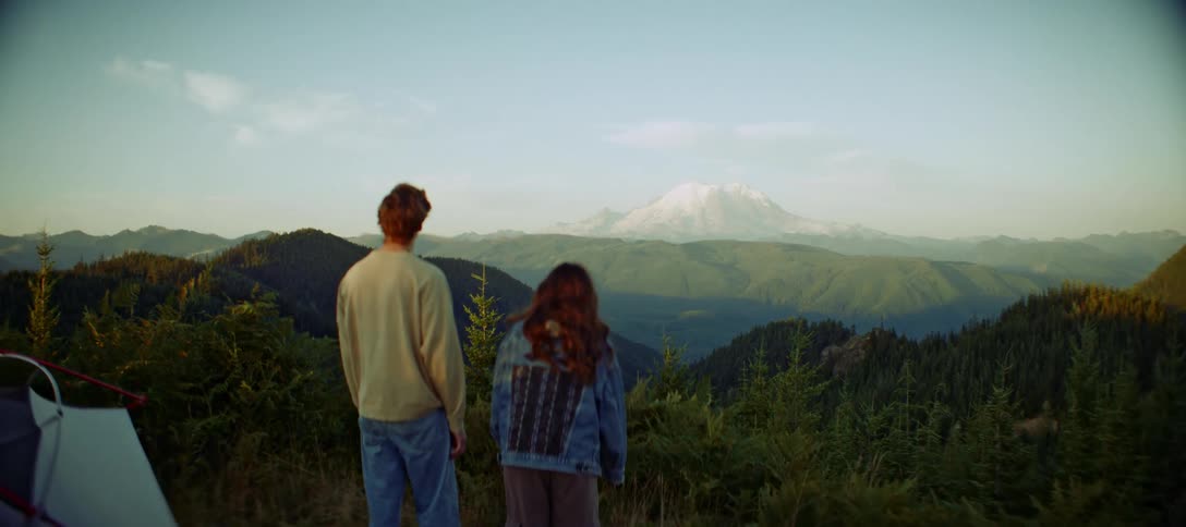 Two people watch a campsite outdoors surrounded by mountains