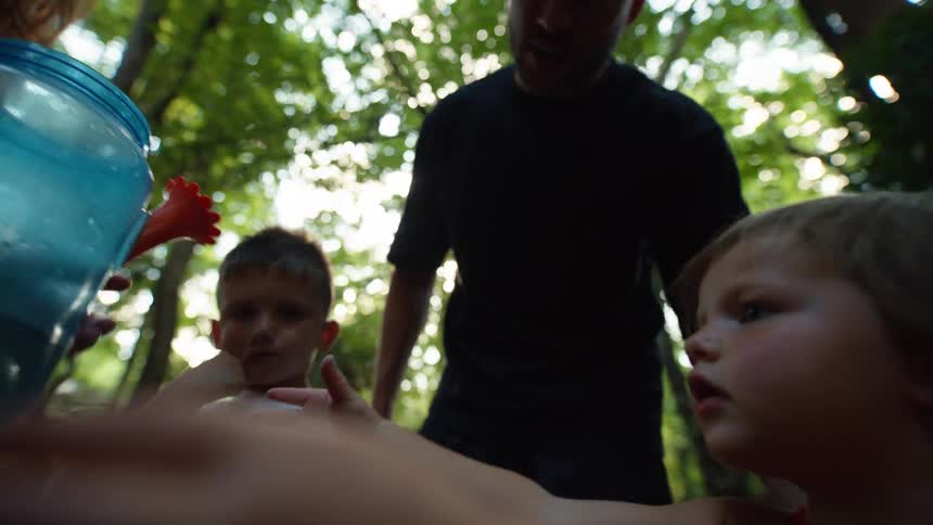 Family outdoors among trees with two children looking at a jug of water